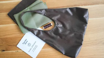 Black bag is lying on a wooden surface next to fabric and instructions.