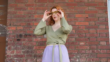 Frau mit Sonnenbrille steht vor einer Ziegelwand.