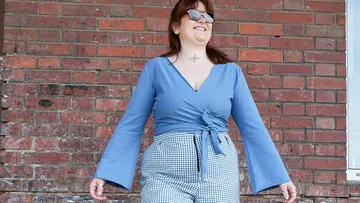 Eine lächelnde Frau trägt eine blaue Bluse und karierte Shorts.