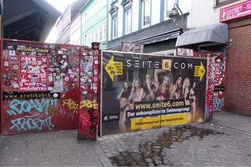 Wand mit Plakat und Aufklebern, zeigt Werbung für Erotik.