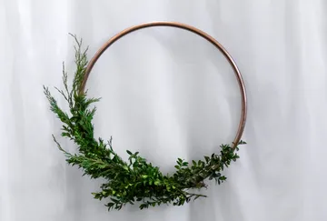 Metal circle with green leaves hanging against a background.