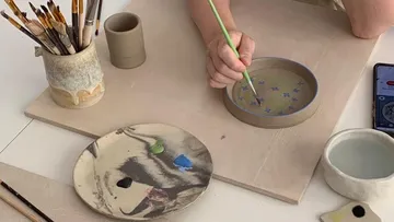 Eine Hand malt mit einem Pinsel auf einer Schale.