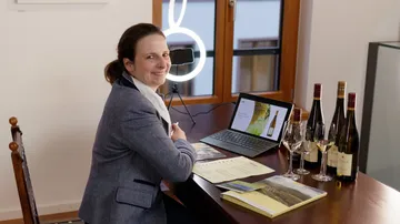 Frau sitzt am Tisch, präsentiert Weine und Daten.