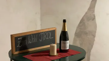 Tisch mit Sektflasche, Kerze und Tafel in dimmer Umgebung.