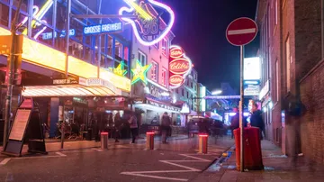 Colourful neon lights illuminate a lively street scene at night.