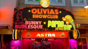 Neon-lit entrance sign of an entertainment club with various offers.