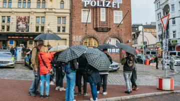 Group of people with umbrellas stand in front of police buildings.