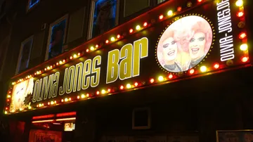 Neon sign shows “Olivia Jones Bar” in a city.
