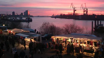 Marktstände erstrahlen im Abendlicht am Wasser.