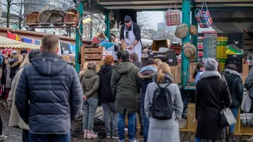 Market table, salesman serving customers, busy outdoor market.
