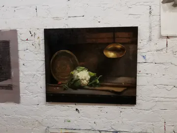 Stillleben mit Blumenkohl und goldenem Löffel an Wand.