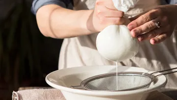 One hand presses a mozzarella over a bowl.