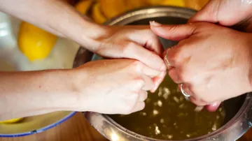 Hands squeeze lemons in a bowl of liquid.