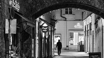 A person walks through an illuminated city alley.