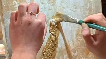 Hände malen mit Pinsel goldene Farbe auf Leinwand.