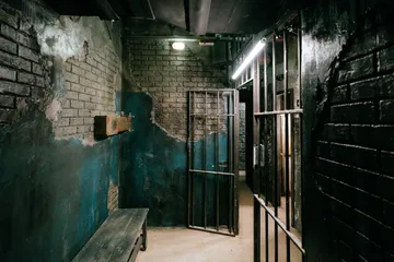 Dark room with open prison doors and a bench.