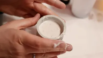 Hände halten einen Behälter mit pastösem Material.