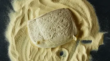 The piece of dough lies on yellowish traces of flour on a black background.