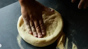 One hand presses dough onto a smooth surface.