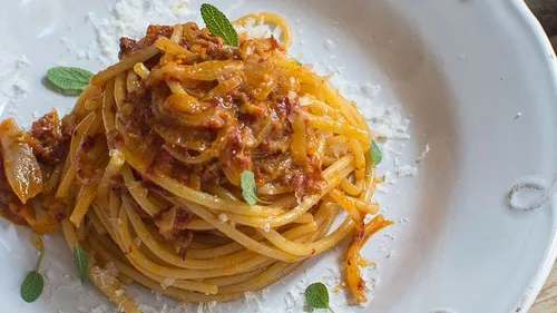 Spaghetti auf einem Teller, umgeben von Soße und Kräutern.