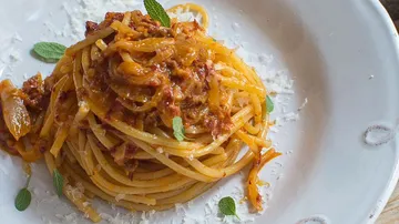 Pasta on a plate, garnished with sauce and herbs.