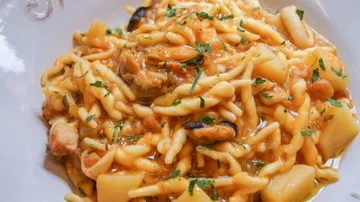 Ein Teller Pasta mit Gemüse und Kräutern in Sauce.