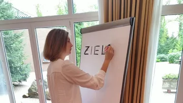 Frau schreibt „ZIEL“ auf ein Flipchart in einem Raum.
