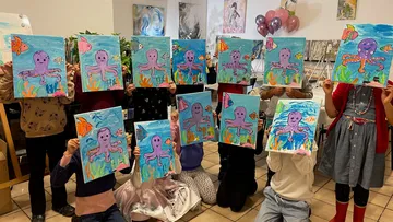 Zwölf Kinder zeigen stolz ihre gemalten Oktopus-Bilder.