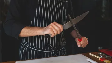 Koch sharpens a kitchen knife in a professional setting.