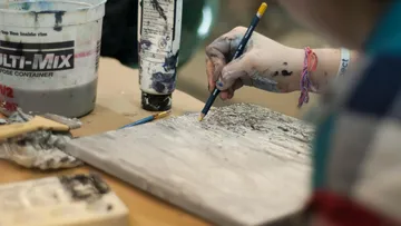 Eine Hand malt mit einem Buntstift auf Holz.