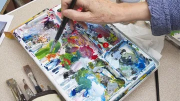 Eine Hand malt mit Pinsel auf einer Farbpalette.