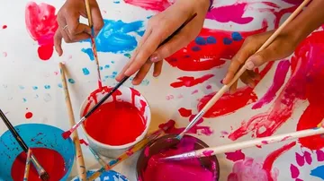 Colored brushes dip into paint containers on a table.