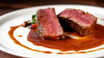 Saftiges Steak auf einem Teller mit Soße und Gemüse.