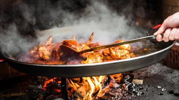 Chicken is cooked over fire in a smoking pan.
