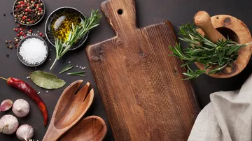 A wooden board with spices and herbs is lying on the table.