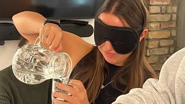 A person pours water from a carafe into a glass.