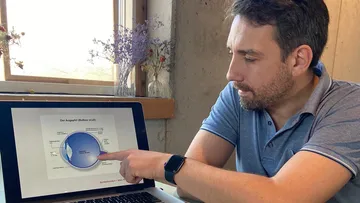 Man points at graphic over his eye on a laptop.