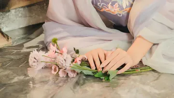 Hands gently touch flowers on a shiny surface.