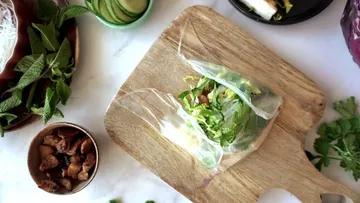 Fresh rice paper roll filled with herbs on wooden board