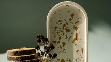 Eine ovale Schale steht neben Holzscheiben und Trockenblumen.