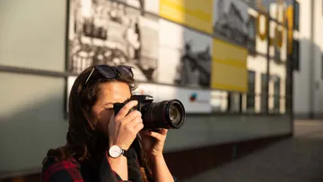 Eine Frau fotografiert vor einer Wand mit Bildern.