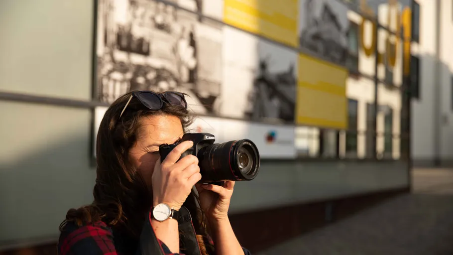 Eine Frau fotografiert vor einer Wand mit Bildern.