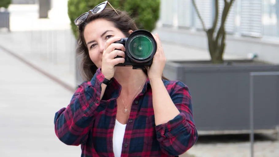 A woman is holding a camera and smiling outdoors.