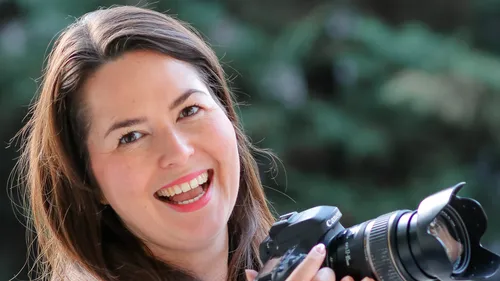 Smiling woman holding camera against green background.