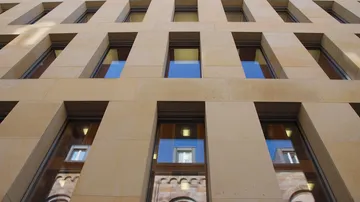 Rechteckige Fenster reflektieren die Umgebung an einer Fassade.