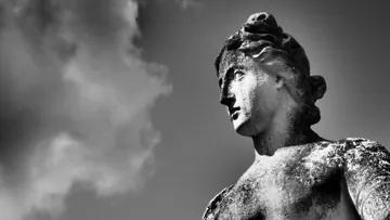 Skulptur schaut nach oben, vor wolkenverhangenem Himmel.