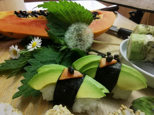 Avocado-Sushi, garniert mit Blüten, Blättern und Papaya.