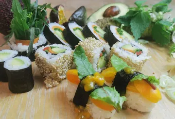 Sushi liegt auf einem Holzbrett, umgeben von frischen Zutaten.
