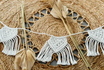 White macrame cape hangs over a woven surface.