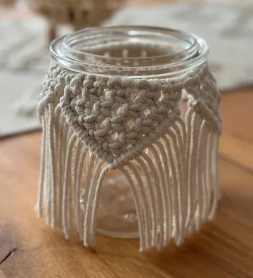 Glass jar with decorative macrame case on wooden table.